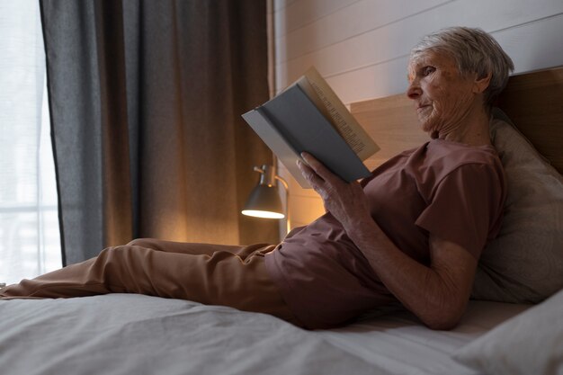 Full shot senior woman reading in bed