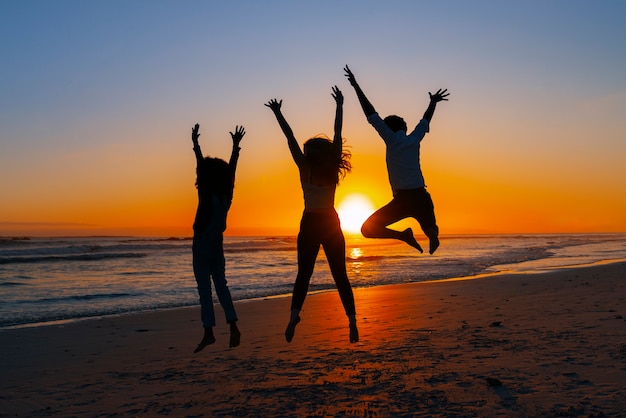 Full shot  silhouettes of people jumping at sunset