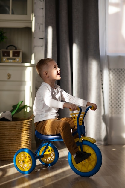 Full shot smiley kid with tricycle indoors