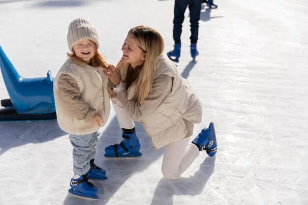 Foto madre e ragazza di smiley del colpo pieno alla pista di pattinaggio