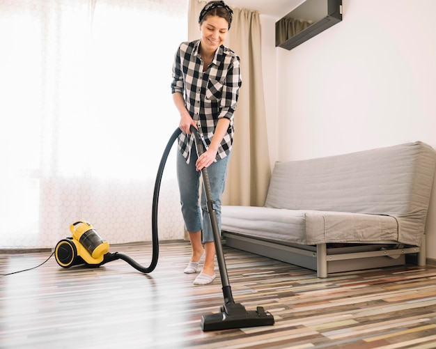 Full shot smiley woman vacuuming