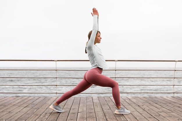 Foto donna del colpo pieno che fa yoga al mare
