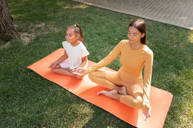 Full shot woman and kid meditating outdoors