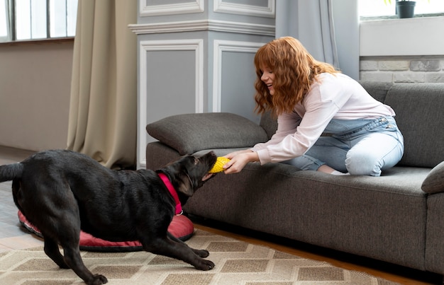 Donna piena del colpo che gioca con il cane a casa