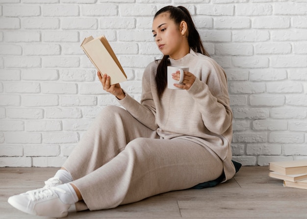 Full shot woman with book and cup  on floor