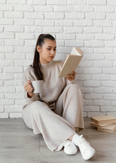 Donna piena del colpo con il libro e la tazza