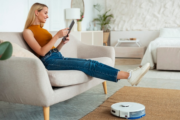 Foto donna a figura intera con aspirapolvere robotico a casa