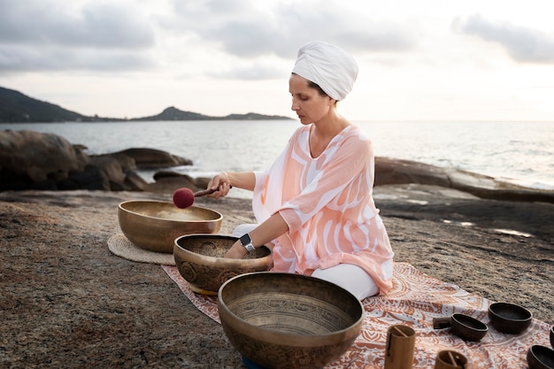 full shot woman with singing bowls outdoors