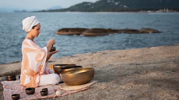 full shot woman with singing bowls at seaside