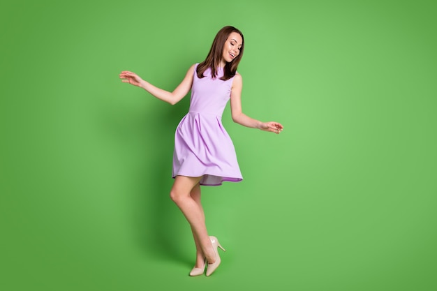 Full size photo adorable sweet careless girl lady look down hands side prom party dress air blow slim legs shoe shop advert concept wear purple dress isolated pastel green color background