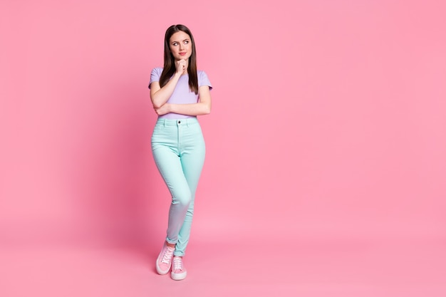 Full size photo of attractive skinny charming lady good mood look side up empty space creative smart person wear casual violet t-shirt teal pants shoes isolated pink pastel color background