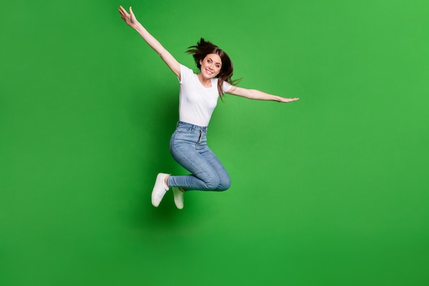 Full size photo of cheerful girl jump hold hands plane fly game concept isolated over green color background