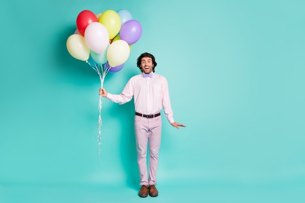 Full size photo of happy impressed guy wear formal shirt pants\
bow hold many balloons isolated turquoise color background