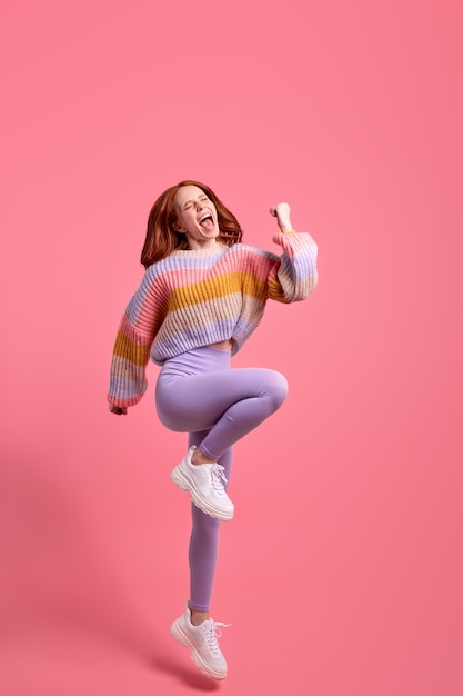 Foto a grandezza naturale di una giovane donna dai capelli rossi felice che urla sì fortunata vittoria alza i pugni salta su indossare casual...