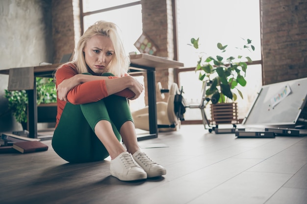 Full size photo of upset woman ceo worker fired sit floor feel lonely solitude have company work startup problems in messy office workplace loft wearing red turtleneck green pants