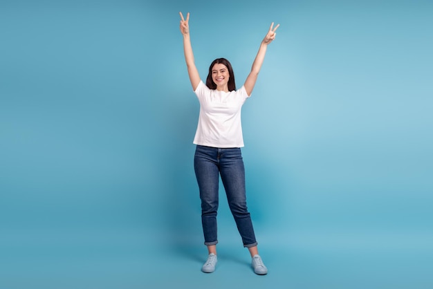 Full size photo of young charming girl have fun show fingers peace v-symbol isolated over blue color background.