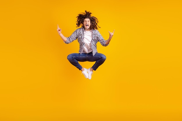 Photo full size photo of young excited guy jump up show fingers rock metal party swag symbol isolated over yellow color background