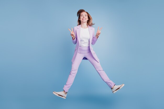 Full size photo of young girl jump show v-sign isolated over blue background