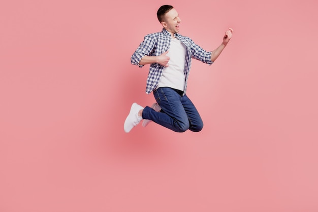 Полноразмерная фотография молодого парня, счастливого и позитивного, улыбающегося, прыгающего, возбужденного, играет на гитаре, изолирована на розовом фоне.