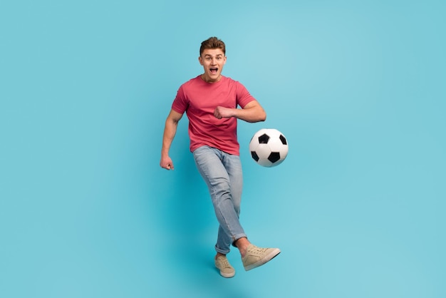 Full size photo of young man play football kick ball team game\
championship isolated over blue color background