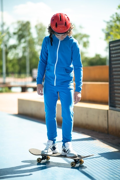 Full-size portrait of a boy in a protective helmet and sports\
suit standing with his both feet on the skateboard