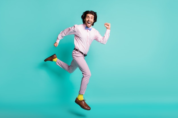 Полноразмерный портрет напуганного бегущего человека, прыгающего высоко одетым в формальную одежду, желтые носки, изолированные на бирюзовом цветном фоне
