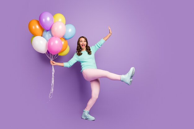 Full-size portret van grappig vrouwelijk meisje geniet van gelegenheid, viert de verjaardag van haar vriend, houdt veel luchtballonnen, schreeuw, draagt pastel zachte trendlaarzen.