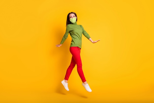 Full size profile photo of funny lady jump up walking wear mask green pullover sneakers trousers isolated yellow color background