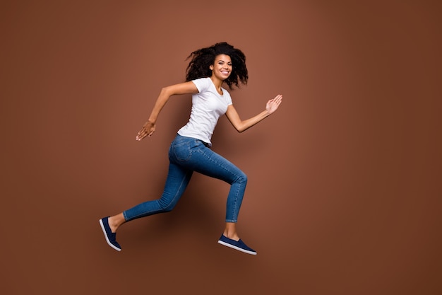 Full size profile portrait of amazing dark skin lady jumping high sports competitions rushing finish line winner mood wear casual white t-shirt jeans.