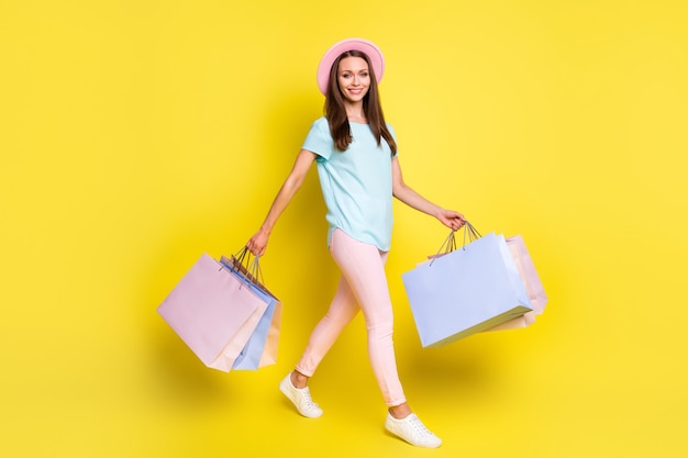 Full size profile side photo positive tourist girl go walk copyspace buy shopping off-sales purchase hold bags wear blue pink t-shirt pants trousers isolated bright shine color background