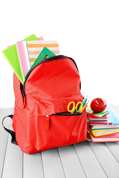 Photo full of stationary red backpack and pile of books with apple on top on wooden table against white background