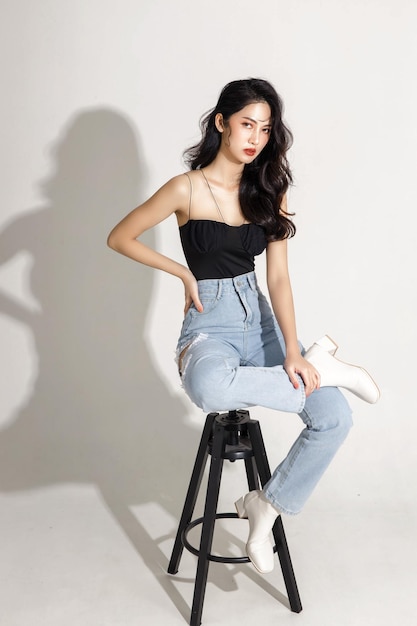 Full street fashion Slender figure beautiful face graceful girl sitting on isolated white background Portrait of female model in studio plastic surgery and aesthetic cosmetology