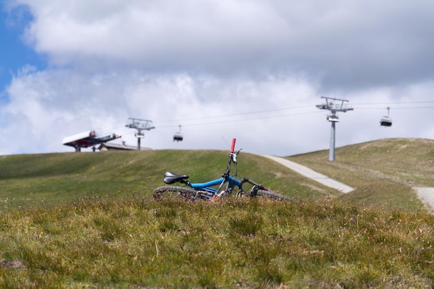 Full suspension downhill mountain bike lying on ground mountains over Livigno with cableway in backround sunny summer day Italy