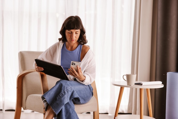 Full view of business woman sitting in chair in room looking at phone