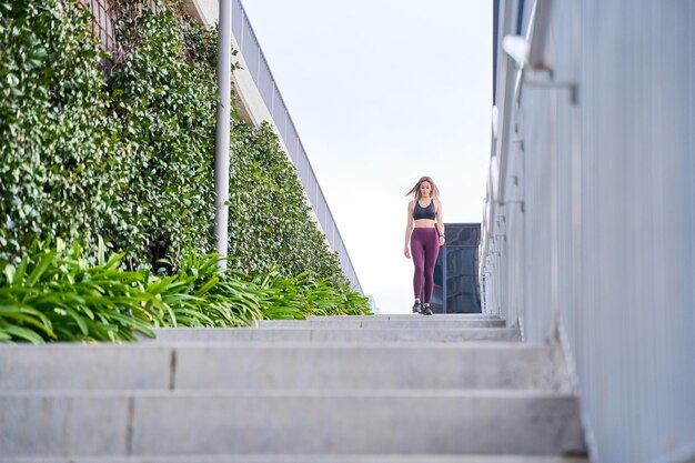 полный вид фитнес-женщины в спортивной одежде, спускающейся по лестнице