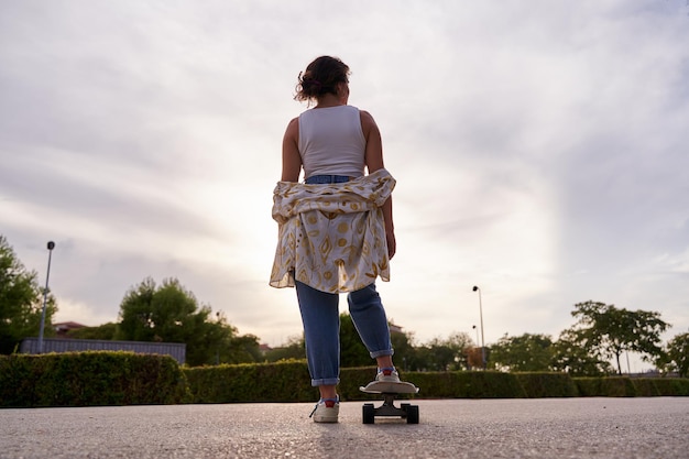 夕暮れに立っているスケートボードの上で認識できない女性の完全な景色