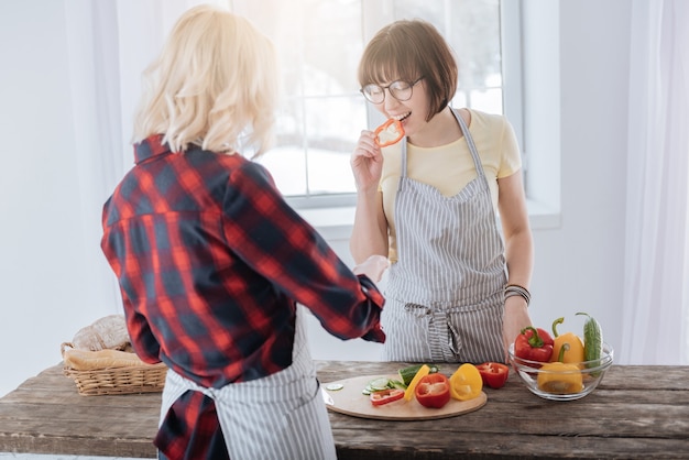 비타민이 가득합니다. 좋은 분위기에있는 동안 부엌에 서서 후추를 먹는 즐거운 매력적인 좋은 여자