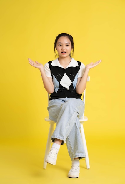 fullbody image of asian girl sitting and posing on yellow background