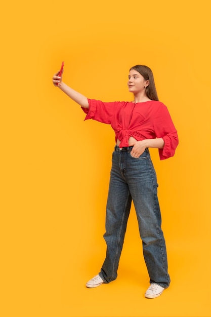 Fullleigh portrait of teenager with phone on bright yellow background Young girl takes selfie of herself Schoolgirl blogger