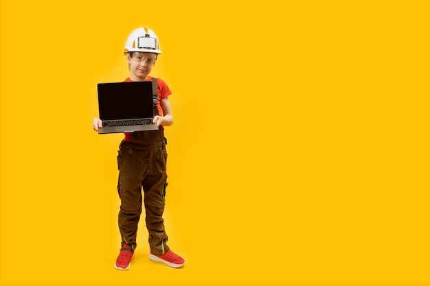 Fullleight portrait of boy holds laptop with empy screen in work clothes and protective helmet child as architect copy space mock up