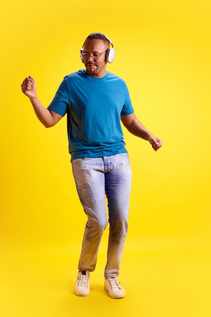 Foto lunghezza completa di un uomo afroamericano in abiti casuali che ascolta musica con le cuffie che si diverte e