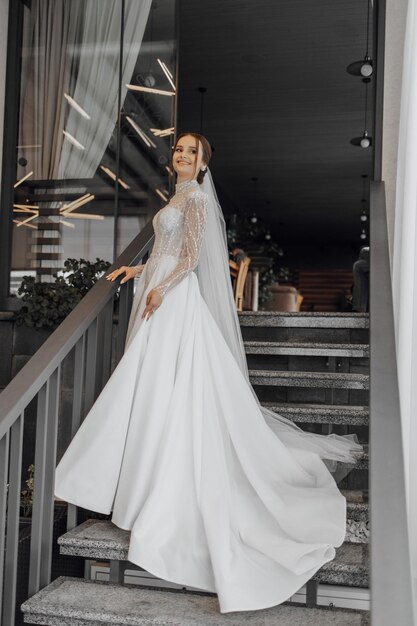 A fulllength bride in a fashionable wedding dress stands on the steps of a restaurant and poses for a photographer wedding day the best event