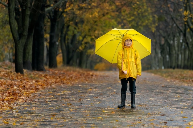 Fulllength del bambino sotto la pioggia sullo sfondo del parco autunnale