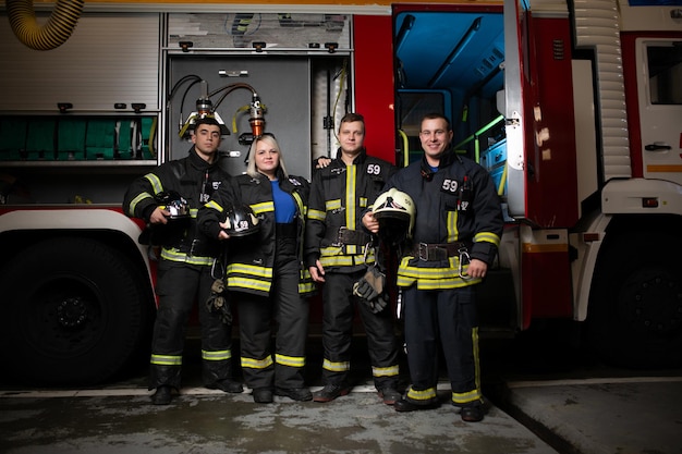 Изображение в полный рост трех пожарных мужчин и женщины на фоне пожарной машины
