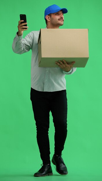 Fulllength male courier holding a box on a green background