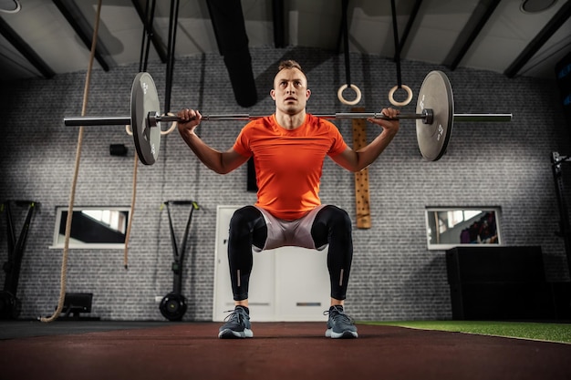 Fulllength photo of a man exercising with a barbell gym