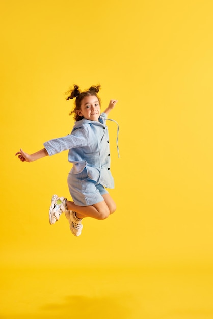 Fulllength portrait of active little kid girl child in casual clothes cheerfully jumping against