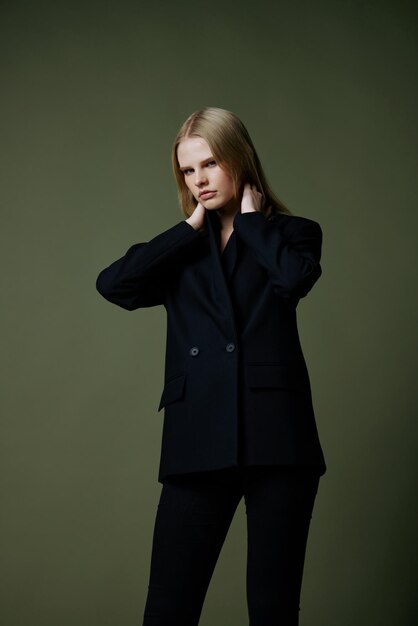 Fulllength portrait of a blonde in a classic suit posing on a green background in the studio