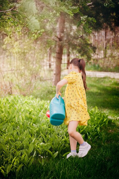 Fulllength portrait of a girl watering lilies of the valley from a watering can a back view of a gir...