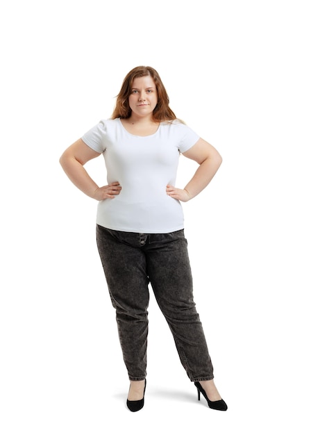 Fulllength portrait of plussize woman wearing white tshirt and jeans posing isolated on white studio